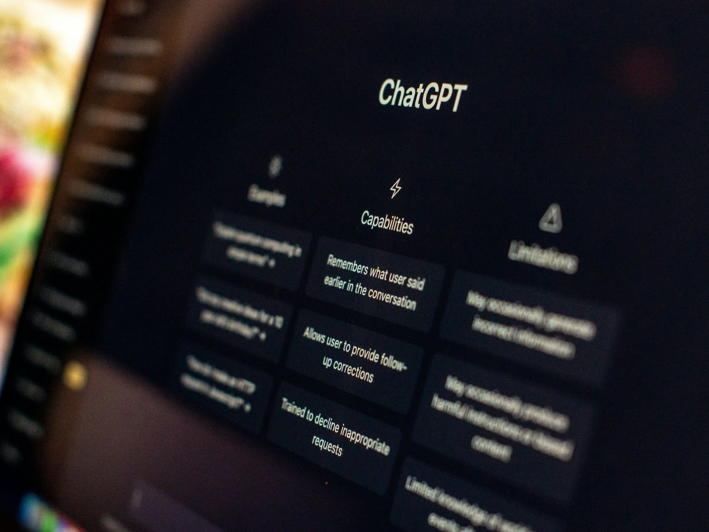 Экран ноутбука крупным планом под углом с открытым интерфейсом ChatGPT — разделы Capabilities и Limitations, на переднем плане размытые цветные блики