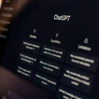 Экран ноутбука крупным планом под углом с открытым интерфейсом ChatGPT — разделы Capabilities и Limitations, на переднем плане размытые цветные блики