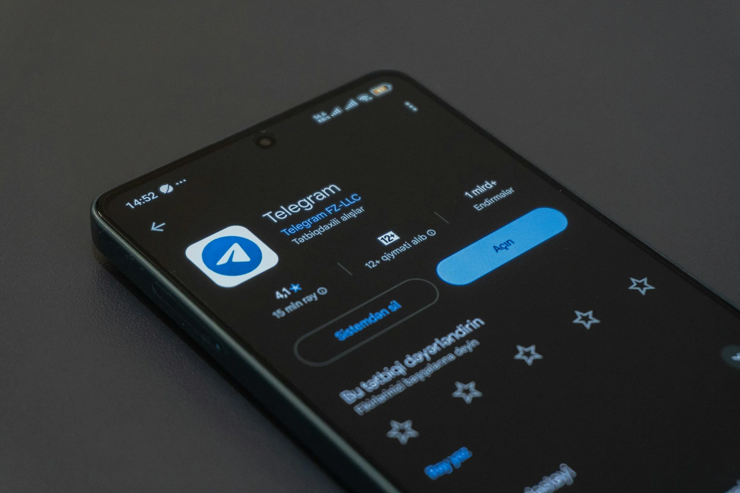Смартфон со страницей Telegram в магазине приложений лежит на тёмном фоне