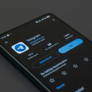 Смартфон со страницей Telegram в магазине приложений лежит на тёмном фоне