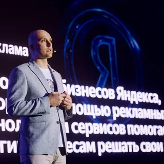 Спикер в сером пиджаке выступает на сцене конференции Яндекс Рекламы на фоне экрана с логотипом «Я Реклама»