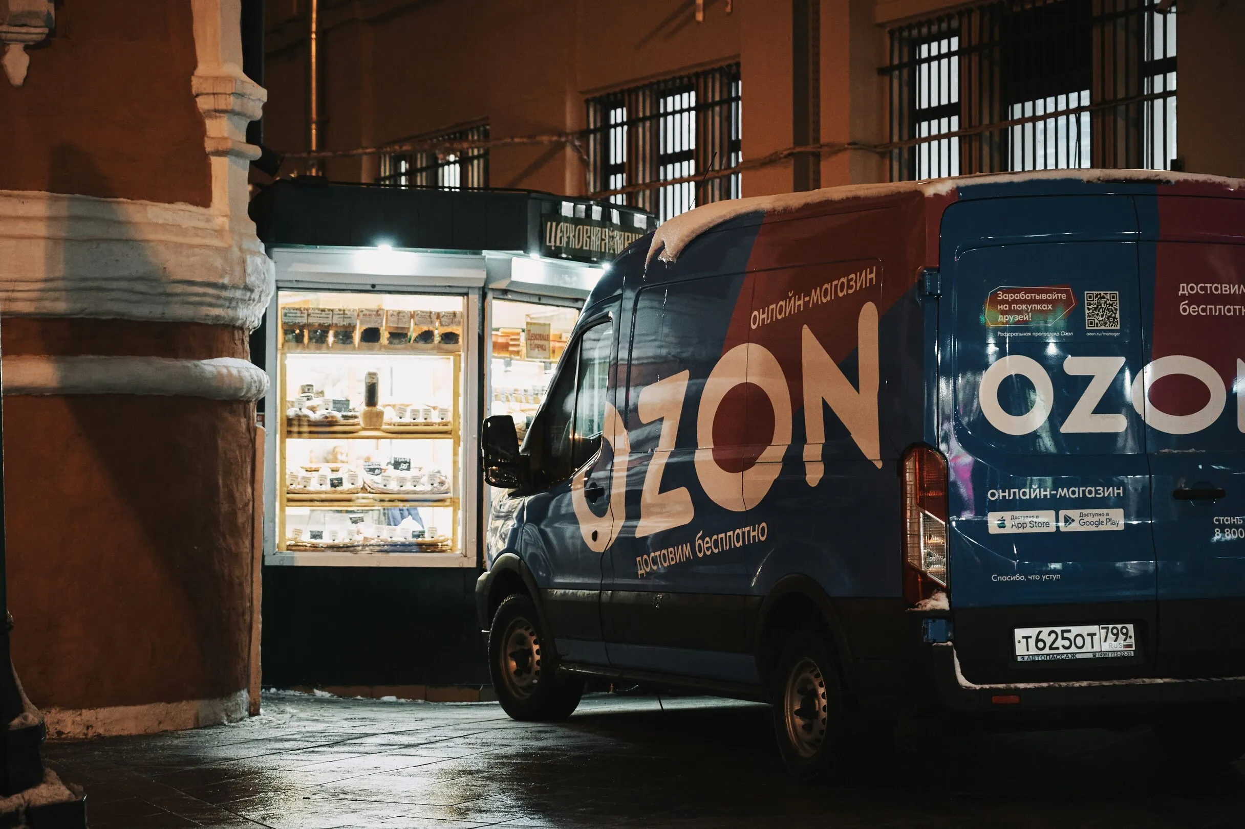 Фургон интернет-магазина Ozon с фирменной надписью припаркован ночью у освещённой лавки